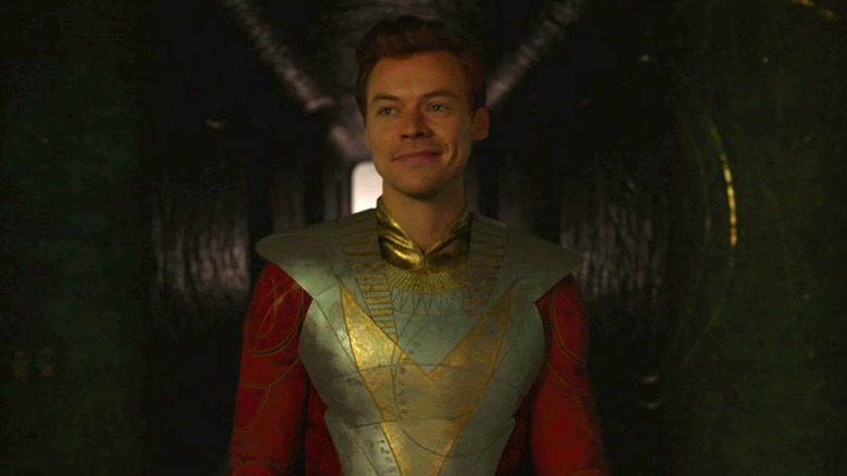 Eros, in gold and red armor, half-smiles in Eternals