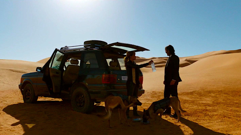 Halle Berry hands Keanu Reeves a bottle of water while standing with her dogs in the desert in John Wick: Chapter 3 - Parabellum