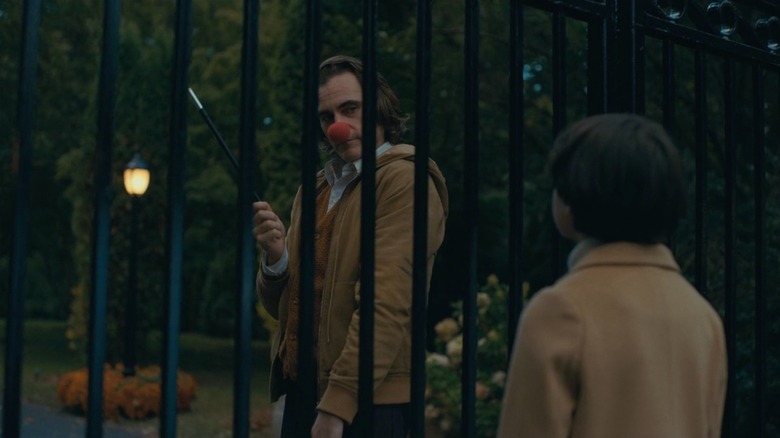 Joker: Arthur with a clown nose, Bruce Wayne behind fence